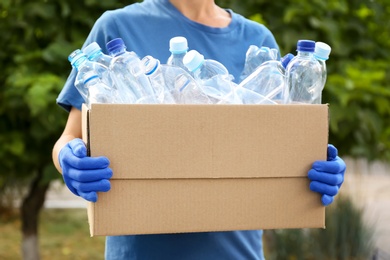 Photo of Woman holding cardboard box with used plastic bottles outdoors, closeup. Recycling problem