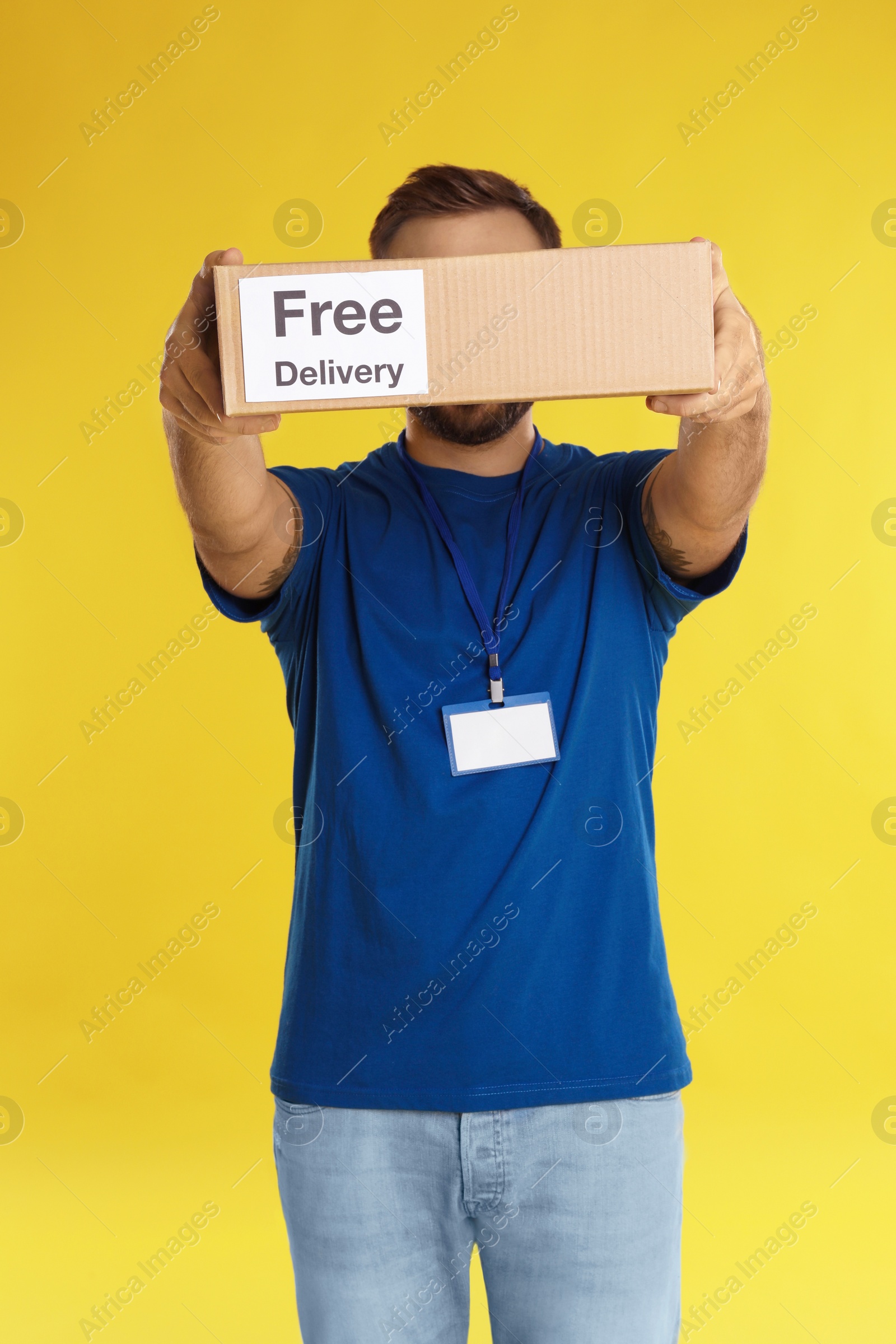 Photo of Male courier holding parcel with sticker Free Delivery on yellow background