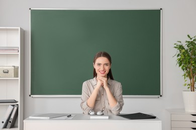 Portrait of beautiful young teacher at table in classroom