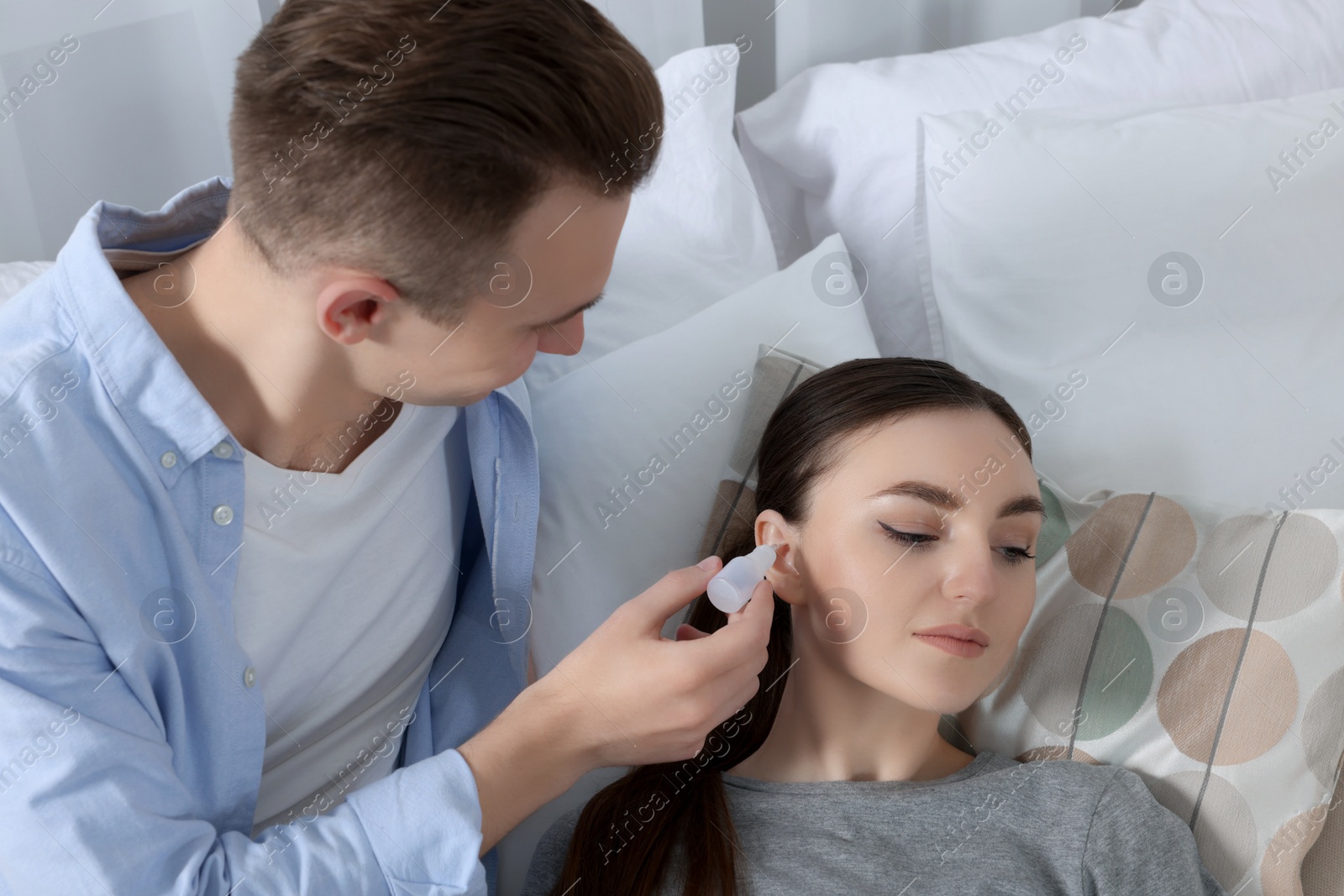 Photo of Man dripping medication into woman's ear at home
