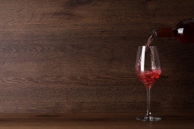 Pouring delicious rose wine into glass on table against wooden background. Space for text