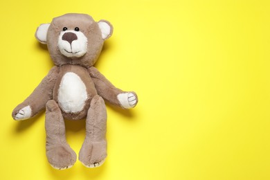 Cute teddy bear on yellow background, top view. Space for text