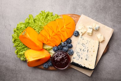 Delicious persimmon, blue cheese, blueberries and jam served on light grey table, flat lay