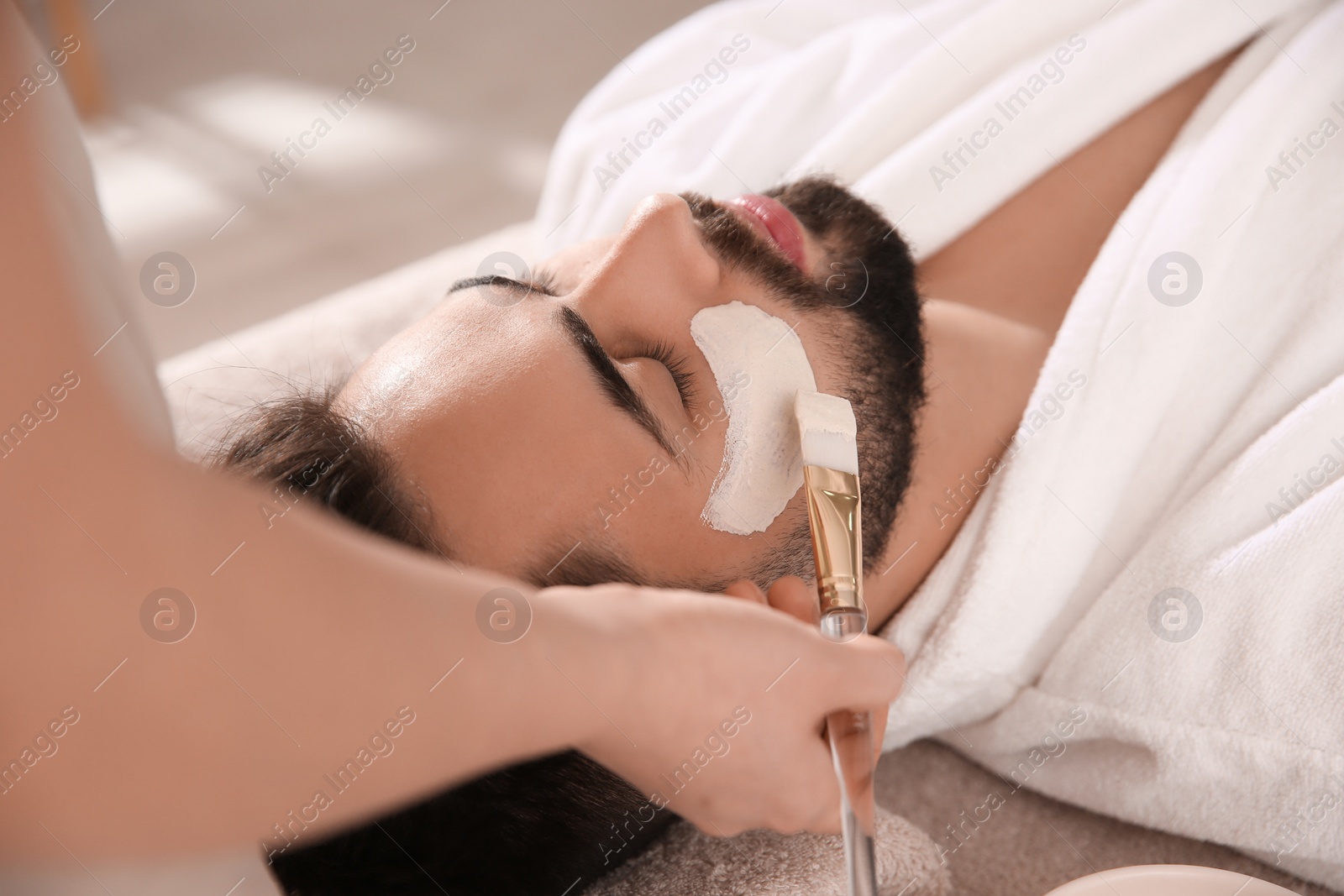 Photo of Cosmetologist applying mask on man's face in spa salon