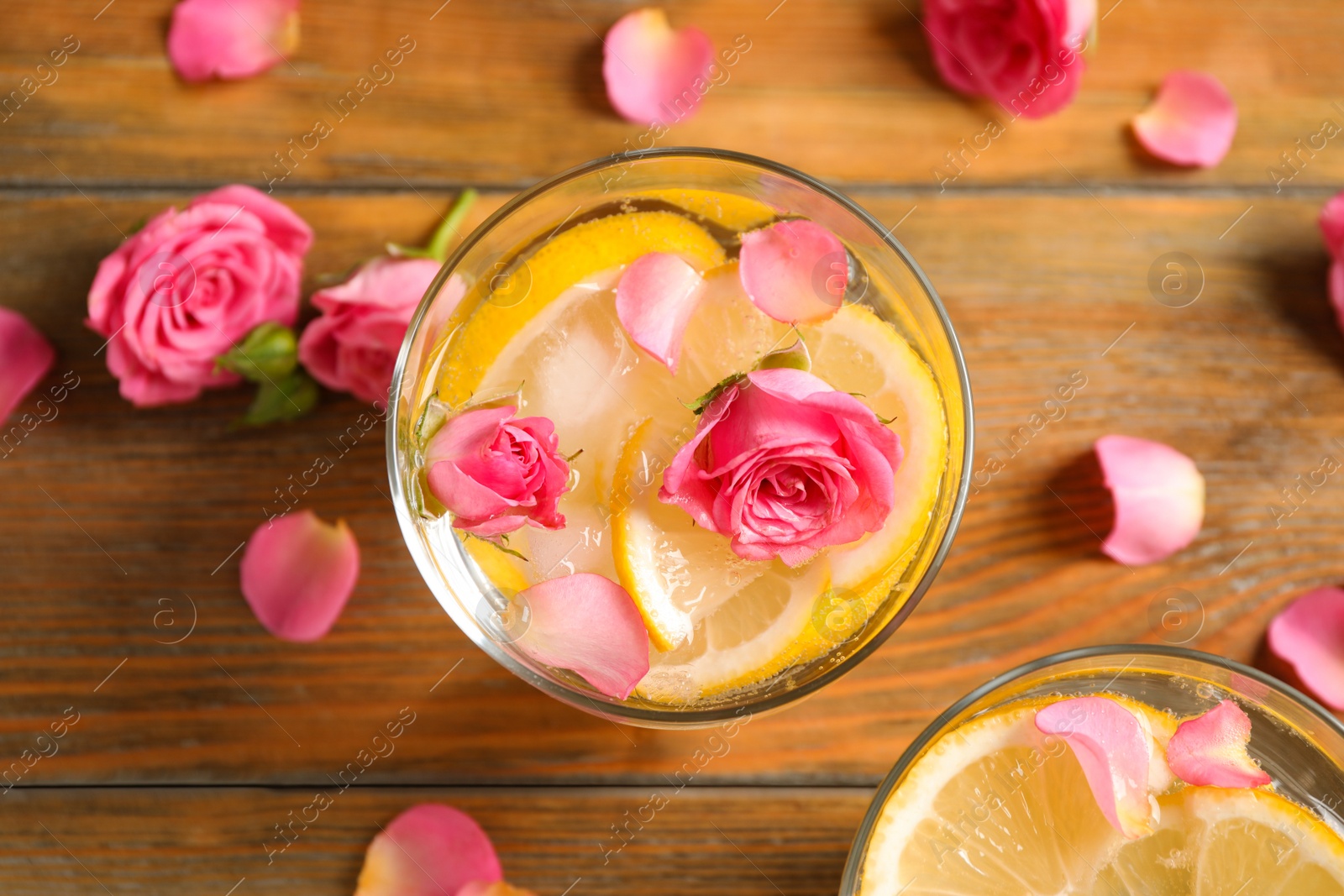 Photo of Tasty refreshing lemon drink with roses on wooden table, flat lay
