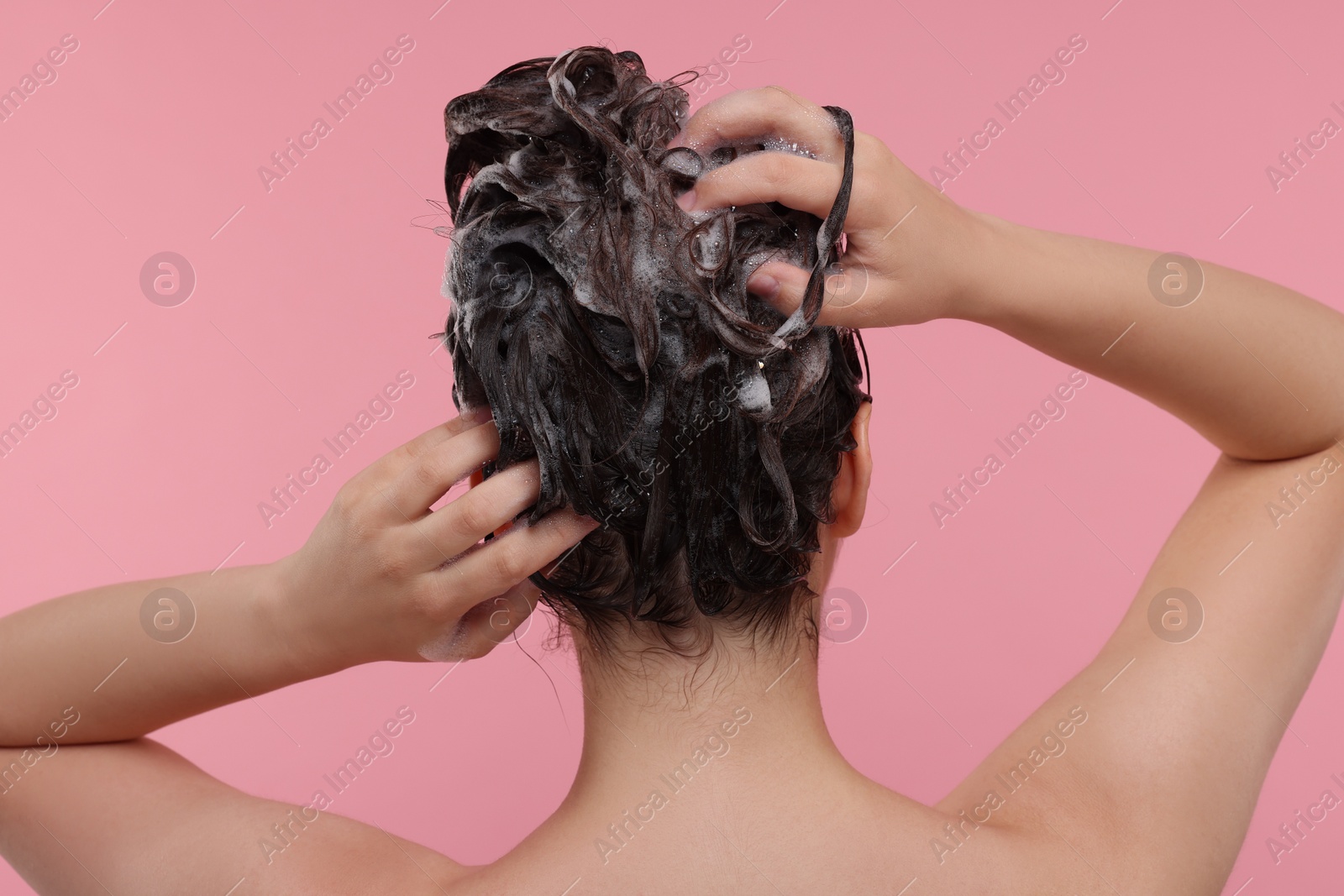 Photo of Woman washing hair on pink background, back view