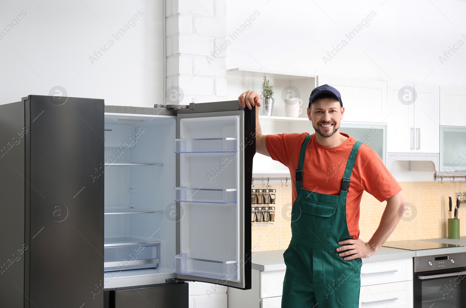 Photo of Male technician in uniform near refrigerator indoors