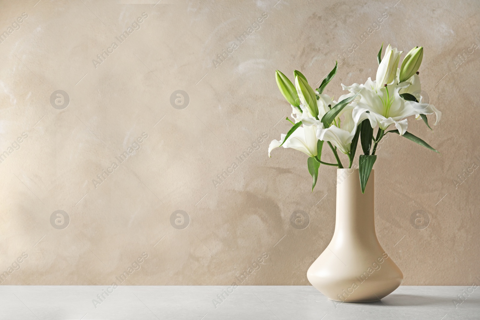 Photo of Vase with beautiful lilies on table against light brown background, space for text