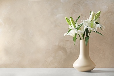 Vase with beautiful lilies on table against light brown background, space for text