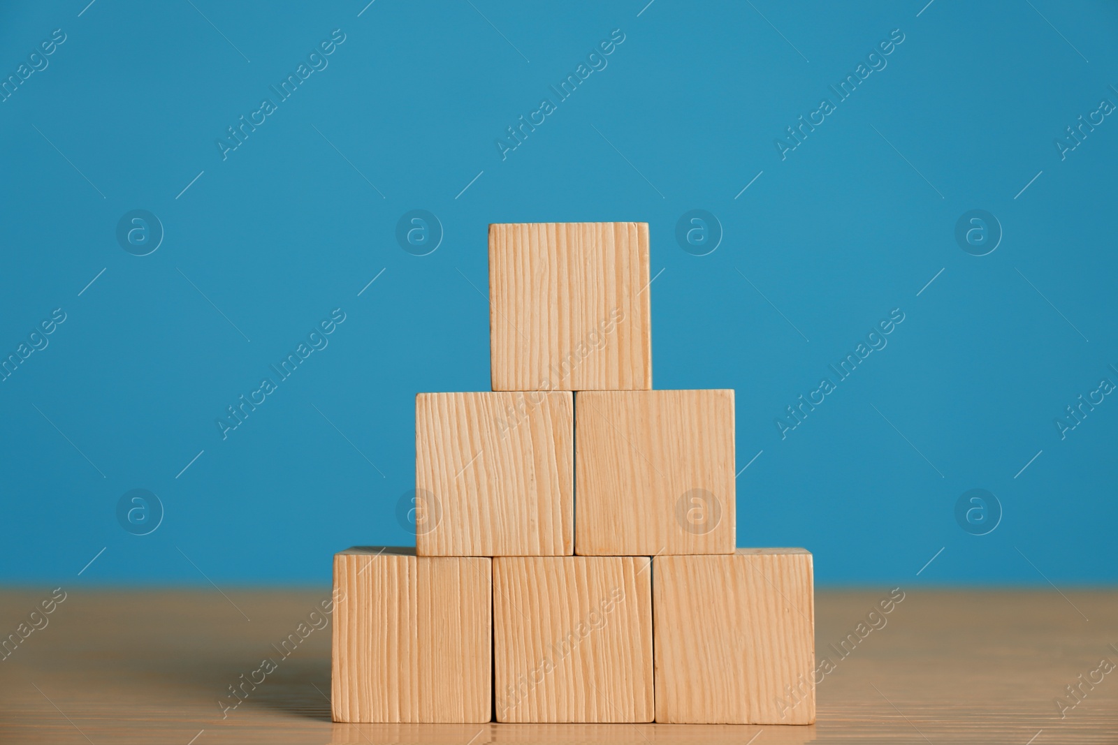 Photo of Pyramid of blank cubes on wooden table against light blue background. Space for text