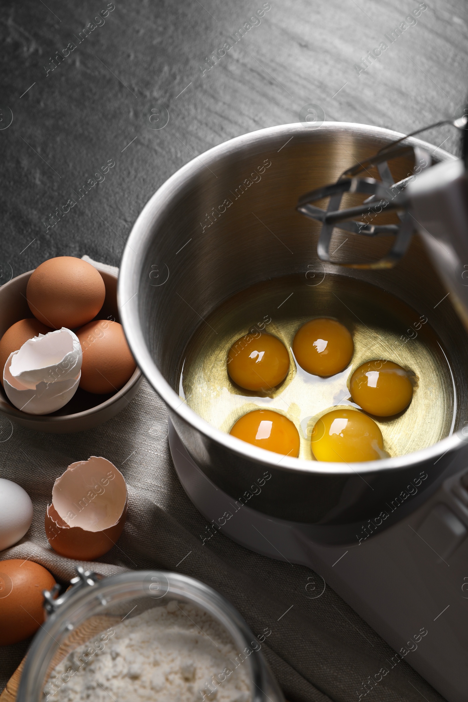 Photo of Making dough. Raw eggs in bowl of stand mixer and ingredients on black table, closeup