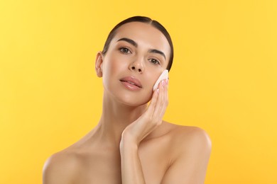 Beautiful woman removing makeup with cotton pad on yellow background