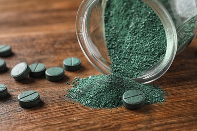 Photo of Jar of spirulina powder and pills on wooden table, closeup