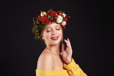 Photo of Beautiful young woman wearing Christmas wreath on black background