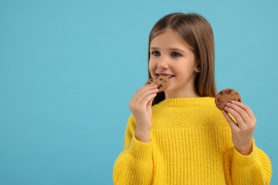 Photo of Cute girl eating chocolate chip cookies on light blue background. Space for text