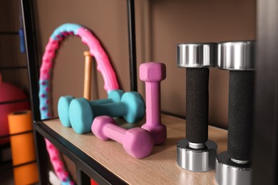 Photo of Different dumbbells on shelf in room with other sports equipment