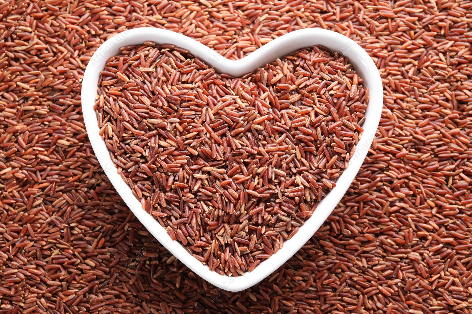 Photo of Pile of brown rice with heart shaped bowl, top view