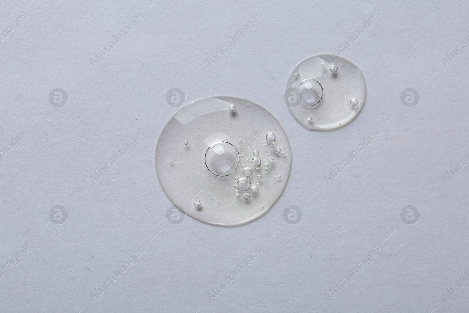 Photo of Drops of cosmetic serum on white background, top view