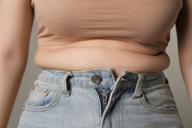 Photo of Overweight woman in tight jeans on grey background, closeup