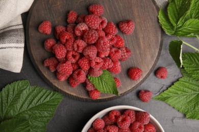 Photo of Fresh ripe raspberries with green leaves on black table, flat lay