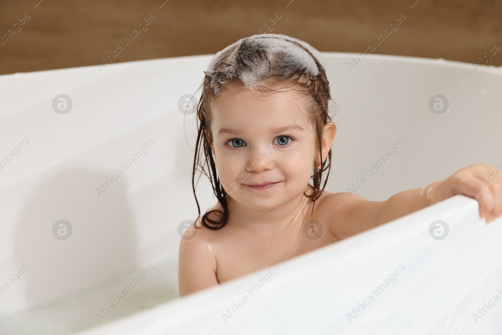 Photo of Cute little girl washing hair with shampoo in bathroom