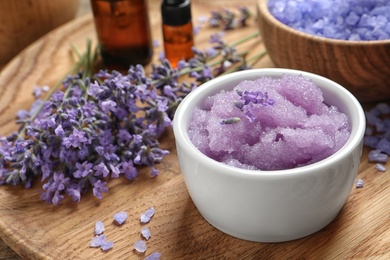 Photo of Bowl of natural sugar scrub and lavender flowers on wooden plate. Cosmetic product