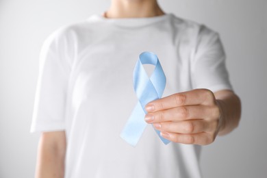 Photo of International Psoriasis Day. Woman with light blue ribbon as symbol of support on white background, closeup