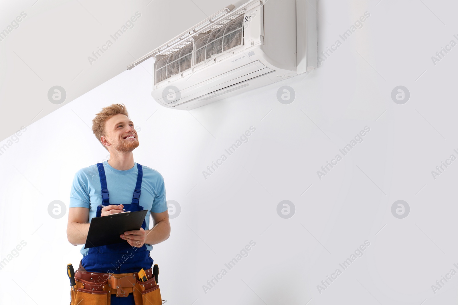 Photo of Professional technician with clipboard near modern air conditioner indoors