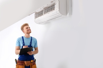 Professional technician with clipboard near modern air conditioner indoors