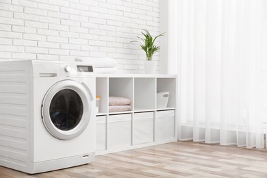 Photo of Modern washing machine near brick wall in laundry room interior, space for text