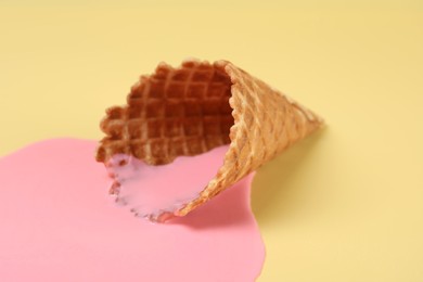 Photo of Melted ice cream and wafer cone on pale yellow background, closeup