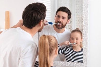 Father and his daughter brushing teeth together near mirror in bathroom