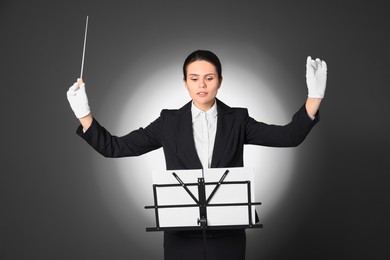 Professional conductor with baton and note stand on grey background