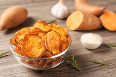 Delicious sweet potato chips in bowl, rosemary and sauce on table. Space for text