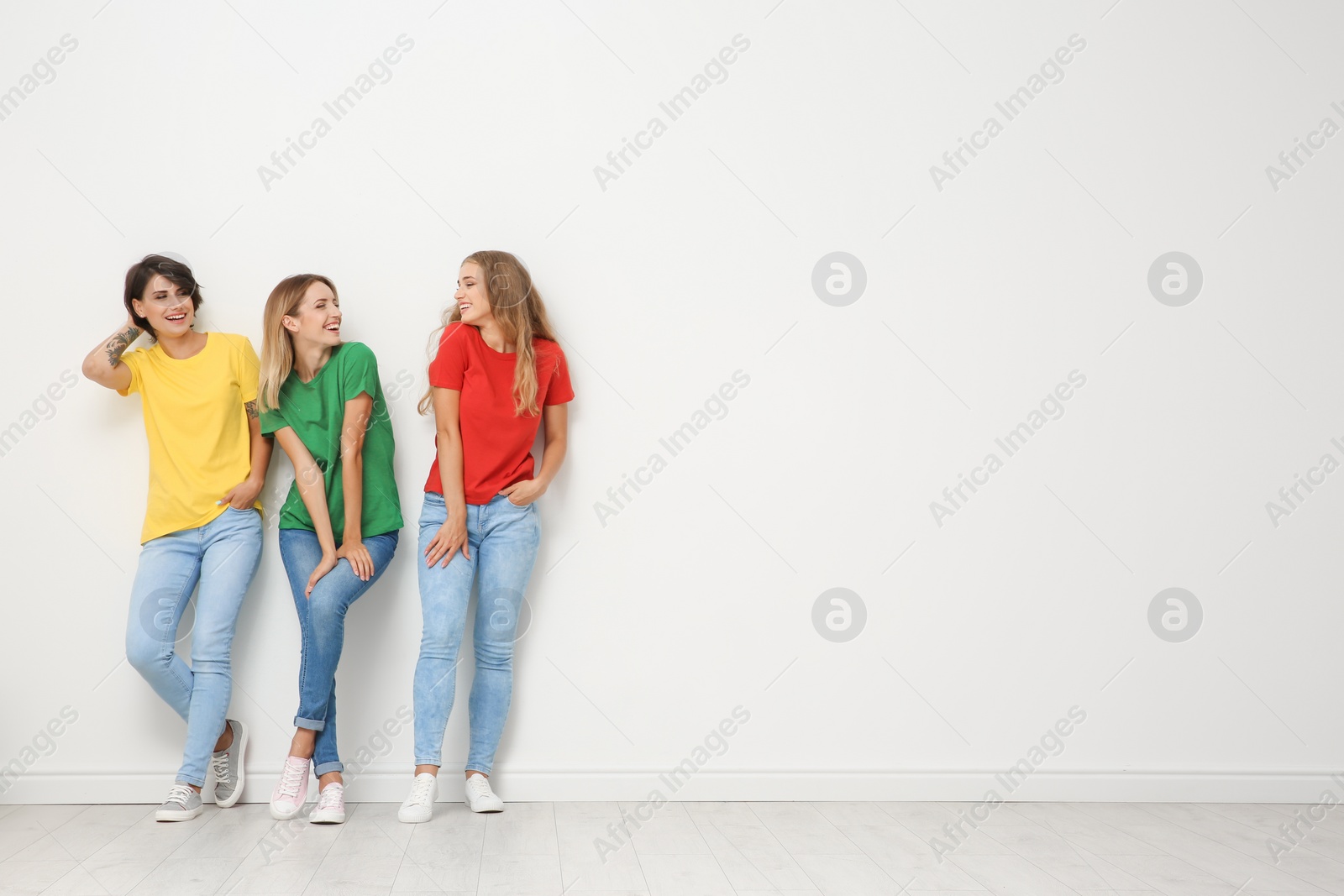 Photo of Group of young women in jeans and colorful t-shirts near light wall