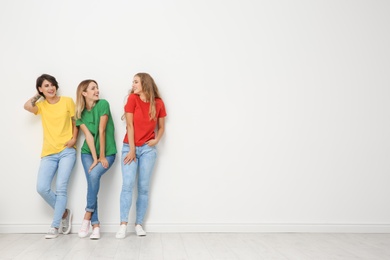 Group of young women in jeans and colorful t-shirts near light wall