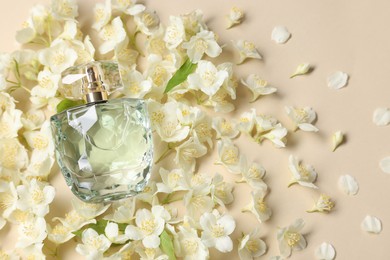 Photo of Bottle of aromatic perfume among jasmine flowers on beige background, flat lay