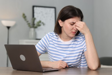 Photo of Overwhelmed woman sitting with laptop at table indoors