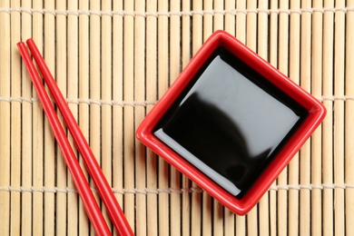 Dish of soy sauce with chopsticks on bamboo mat, flat lay