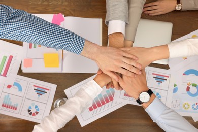 Office employees joining hands at work, top view