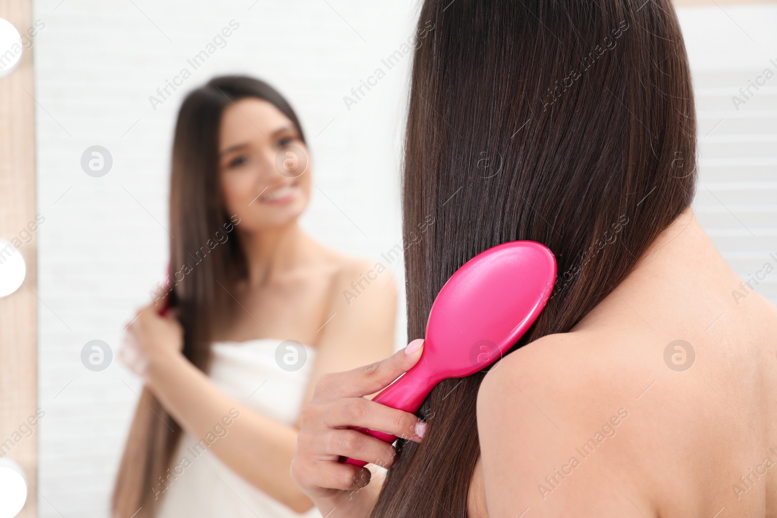 Photo of Beautiful young woman with hair brush looking into mirror in bathroom