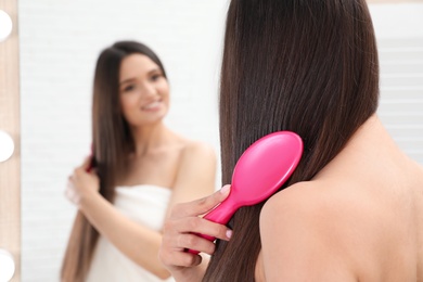 Beautiful young woman with hair brush looking into mirror in bathroom