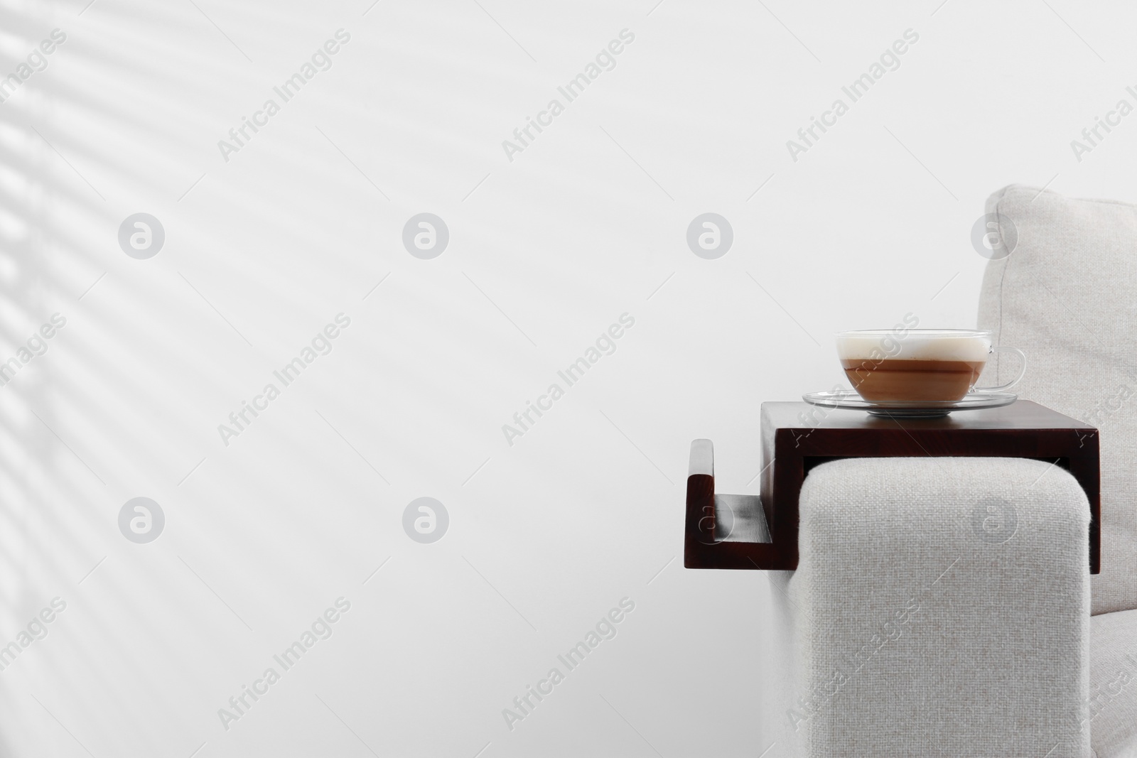 Photo of Cup of coffee on sofa with wooden armrest table indoors, space for text. Interior element