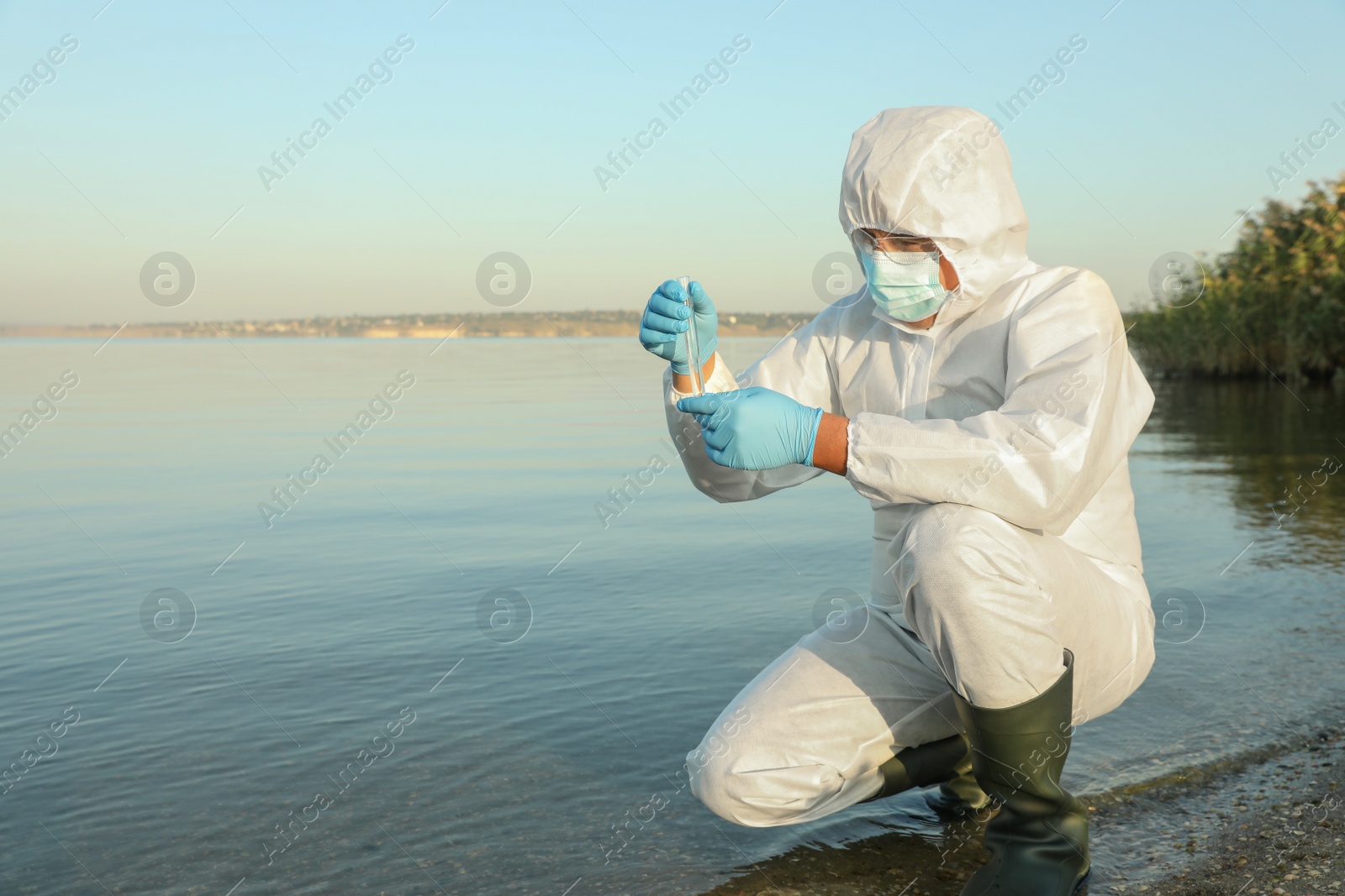 Photo of Scientist in chemical protective suit with test tube taking sample from river for analysis