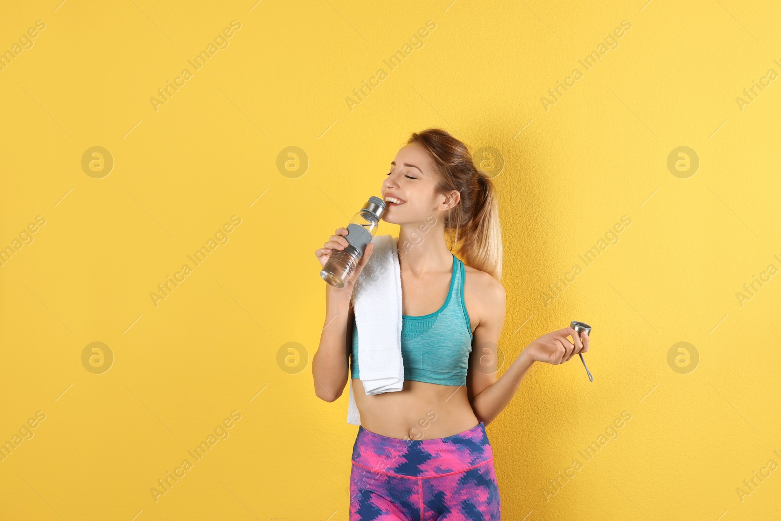 Photo of Beautiful young woman in sportswear with towel and bottle of water on color background