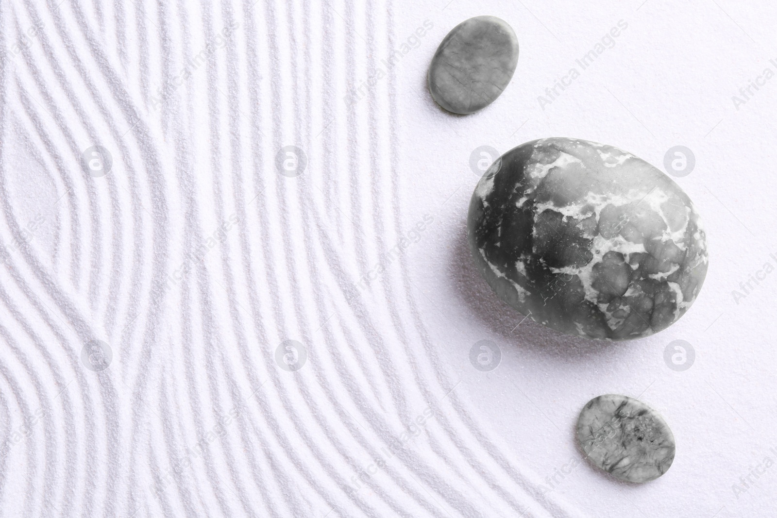 Photo of Zen garden stones on white sand with pattern, flat lay