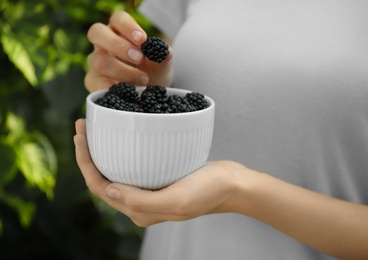 Woman with bowl of tasty ripe blackberries in garden, closeup