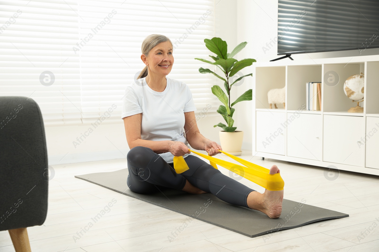 Photo of Senior woman doing exercise with fitness elastic band on mat at home