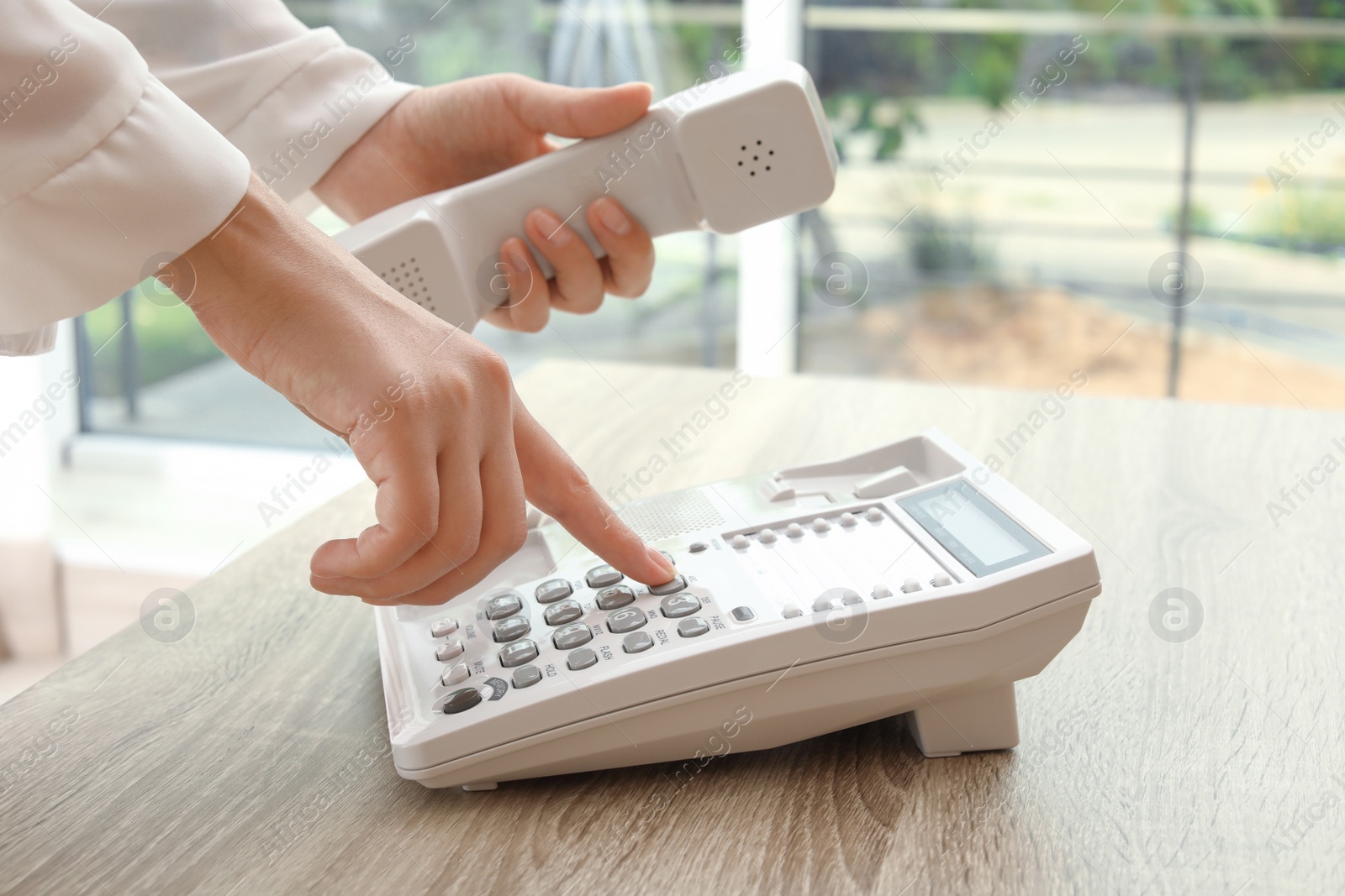 Photo of Woman dialing number on telephone at table indoors, closeup