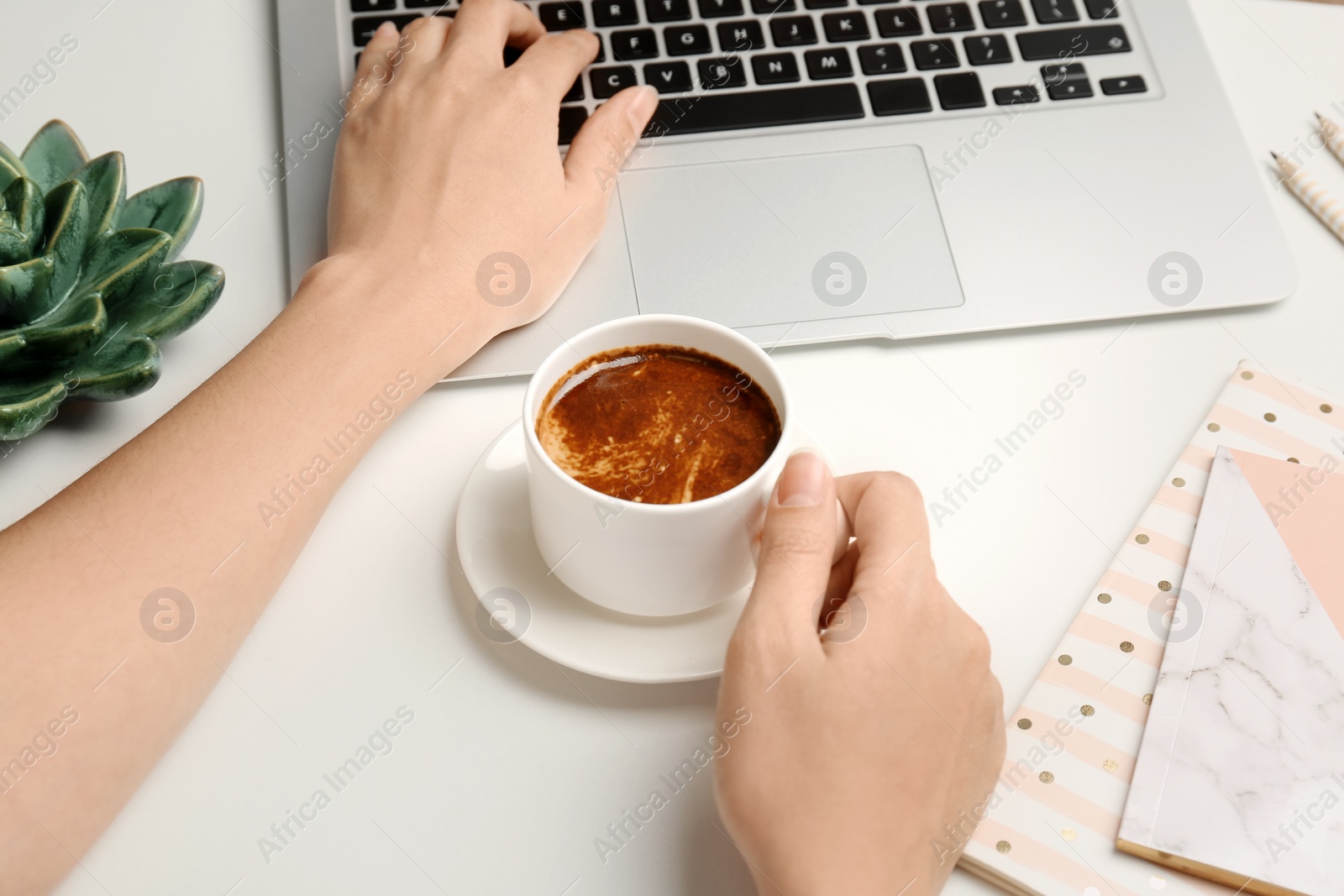 Photo of Young woman with cup of delicious coffee using laptop at table